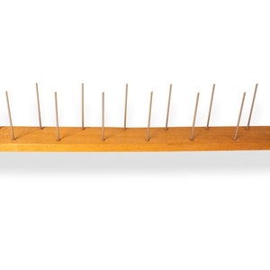 May include: A wooden board with 16 metal pins sticking up from it. The board is light brown and the pins are silver.