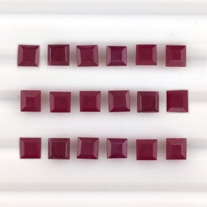 Puede incluir: Dieciséis gemas cuadradas de color rojo intenso están dispuestas en una cuadrícula. Las gemas tienen una superficie pulida y una forma consistente, lo que sugiere que están cortadas del mismo material. El color es un rojo rico y saturado.