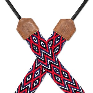 May include: A red, blue, and white woven camera strap with a geometric pattern. The strap has two brown leather ends with the text "The Source" embossed on them.