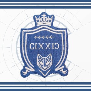 Pode incluir: Um patch bordado azul e branco em forma de escudo, com o texto "CIXXIX" e um rosto de gato geométrico. O patch é encimado por uma coroa e tem uma borda decorativa.