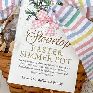 Könnte beinhalten: Ein Weidenkorb mit einem Etikett mit der Aufschrift "Stovetop Easter Simmer Pot". Das Etikett ist mit einer rosa Vichy-Schleife und Lavendelzweigen verziert. Der Korb ist mit einem pastellfarbenen Streifenband gebunden.