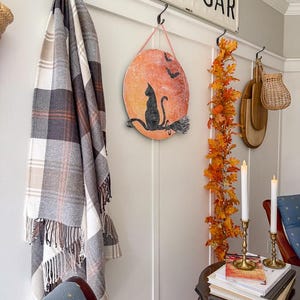 DIY black cat Halloween sign on a fall gallery wall with a plaid throw, autumn leaf garland and brass candlesticks