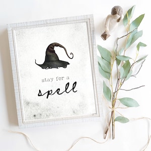May include: A white framed print with a black and white illustration of a witch's hat and the text "stay for a spell".