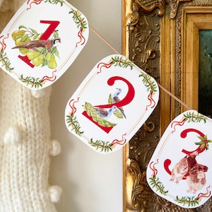May include: A festive banner featuring numbered cards with watercolor illustrations of birds and foliage. Each card has a red number, a decorative border, and is strung on a natural twine. The banner is a charming holiday decoration.