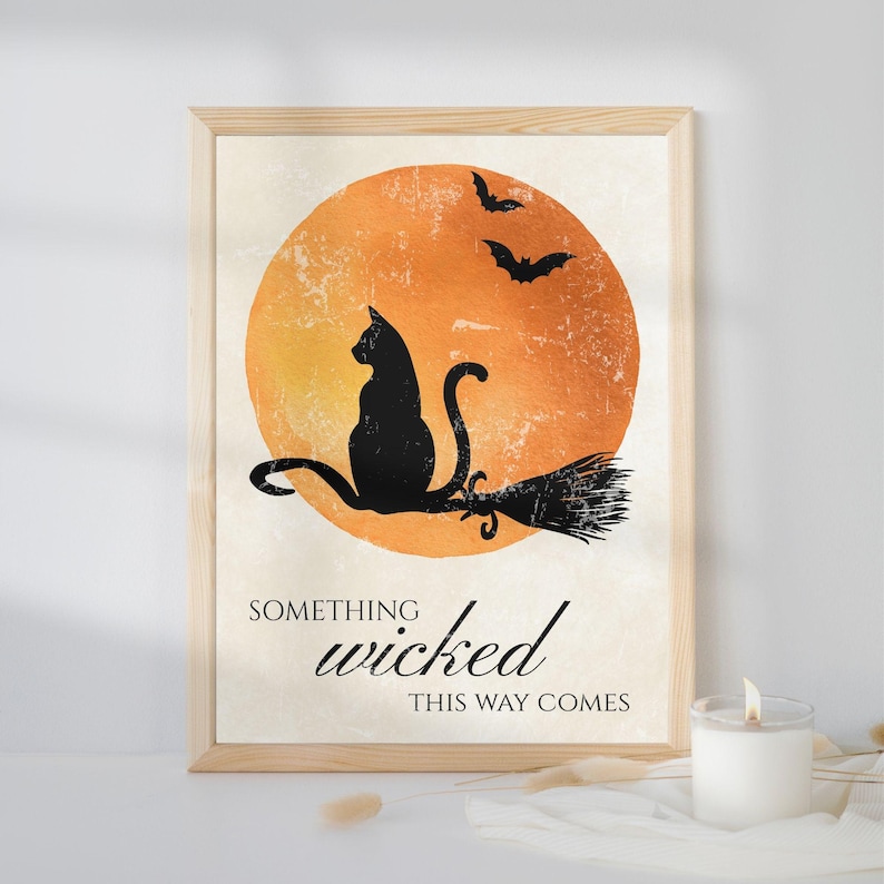 Vintage Halloween wall art with a black cat on a witch's broom and the quote "Something Wicked This Way Comes" in a light wood frame