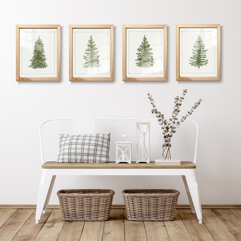 May include: Four framed wall art prints featuring watercolor illustrations of evergreen trees in light wood frames, displayed above a white metal bench with a wooden seat, a plaid pillow, two white lanterns, and two woven storage baskets.