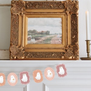 May include: A white and pink Halloween banner with a string of ghost illustrations. Each ghost has a floral crown and is holding a small pumpkin. The banner is hanging on a white mantel.