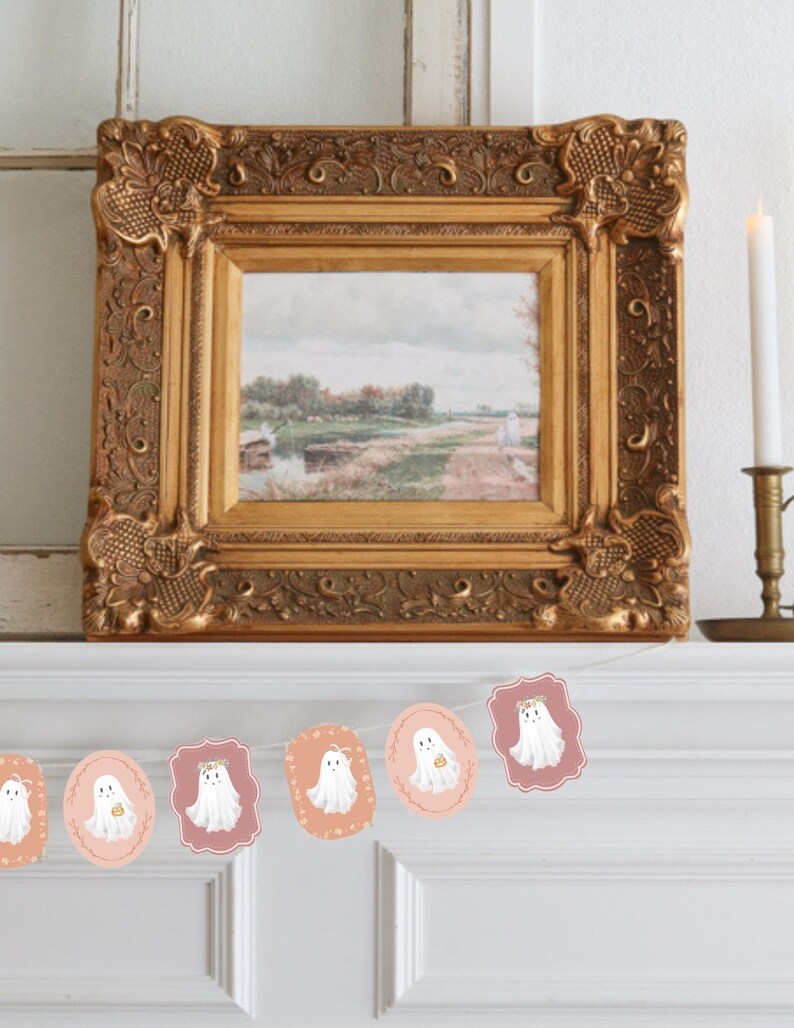 May include: A white and pink Halloween banner with a string of ghost illustrations. Each ghost has a floral crown and is holding a small pumpkin. The banner is hanging on a white mantel.
