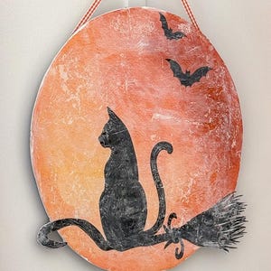 Close-up of a handmade black cat Halloween door hanger with an orange moon, bats and a distressed vintage finish, hung with gingham ribbon