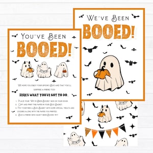 May include: A printable Halloween "You've Been Booed!" sign with instructions on how to play the game. The sign features a ghost holding a pumpkin and bats flying around. The text says "We hope you enjoy your spooky Boo and that you'll surprise a friend too! Here's what you've got to do: 1. Place your 'We've Been Booed' sign on your door. 2. Copy and print this paper in your Boo Basket. 3. Put together a Boo Basket with some special treats and goodies along with the paper you printed. 4. Boo a friend who hasn't been Booed yet!"