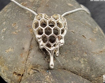 May include: Silver necklace featuring a heart-shaped pendant that resembles a honeycomb dripping with wax. The pendant is made of metal and has a shiny finish. The necklace is displayed on a grey rock.