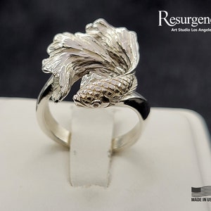 May include: A silver ring featuring a detailed, three-dimensional sculpture of a betta fish. The fish's fins are spread out, and its body is textured. The ring is made in the USA.