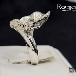 May include: A silver ring featuring a detailed mermaid tail design. The ring is made in the USA.