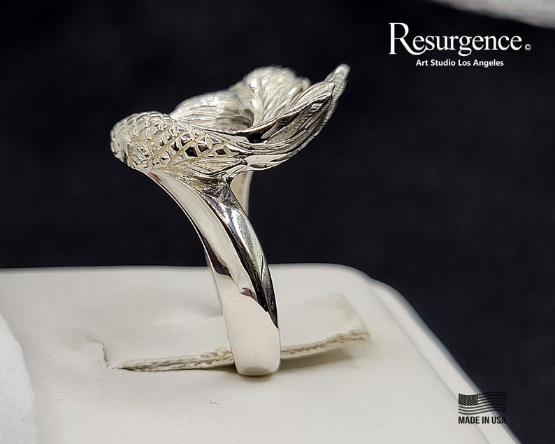 May include: A silver ring featuring a detailed mermaid tail design. The ring is made in the USA.