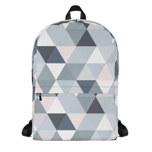 Puede incluir: Una mochila de color gris y blanco con estampado geométrico y detalles en rosa. La mochila tiene un bolsillo con cremallera en la parte delantera y correas ajustables.