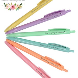 Op de afbeelding: Set van zes pastelkleurige pennen met motiverende citaten erop gedrukt. De citaten zijn: "You're a fucking awesome", "You've got this shit", "Keep going gorgeous", "Work hard, fuck harder", "Dream big beautiful", en "Be fucking kind".