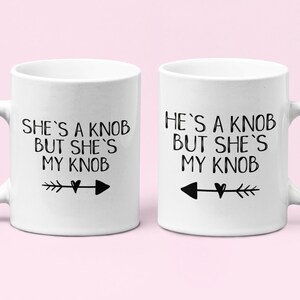 May include: Two white ceramic mugs with black text and arrows. The mug on the left says "She's a knob but she's my knob". The mug on the right says "He's a knob but she's my knob".