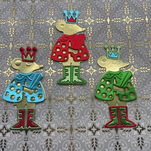 May include: Three whimsical die-cut figures of mice wearing crowns and capes in red, blue, and green. The mice have gold-colored bodies and are posed on a patterned gray background with gold accents. The figures are wearing boots.