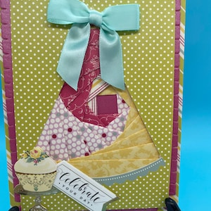 May include: A handmade greeting card with a light blue bow and a cupcake illustration. The card features a green polka dot background and a layered design with various patterned papers. The text "Celebrate your day" is included.
