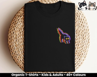 Puede incluir: Camiseta negra con un gráfico de un gato arcoíris. El gato está mirando hacia la derecha y tiene ojos amarillos. La camiseta está hecha de algodón orgánico.