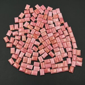 May include: A large collection of small, rectangular pink coral cabochons arranged in a loose cluster. Each piece features a smooth, polished surface with subtle variations in shade, ranging from soft pastel pink to deeper coral tones.