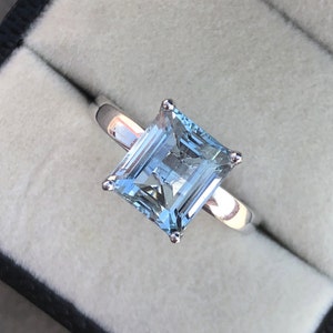 Op de afbeelding: Een zilveren ring met een grote, vierkante aquamarijn edelsteen. De edelsteen is lichtblauw en heeft een facetgeslepen vorm.