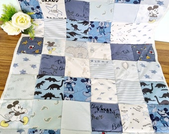Puede incluir: Una colcha de bebé de retazos azul y blanca con temática de Mickey Mouse. La colcha está hecha de varias telas, incluyendo algodón y franela. Presenta una variedad de diseños de Mickey Mouse, incluyendo cabezas de Mickey Mouse, orejas de Mickey Mouse y siluetas de Mickey Mouse. La colcha también presenta las palabras "BRAND NEW LITTLE BROTHER", "MUMMY", "TELL", "DOKER" y "BALKER BY THE PIER".