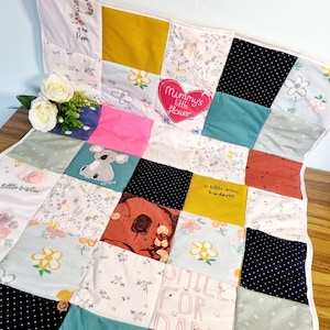 May include: A patchwork baby quilt featuring a variety of fabrics and colours, including green, blue, pink, yellow, and red. The quilt incorporates a range of designs, such as flowers, animals, and words. The words on the quilt include "Mommy's little flower", "a little more kindness", and "smile for daddy".