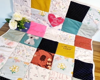 Puede incluir: Una colcha de bebé de retazos con una variedad de telas y colores, incluyendo verde, azul, rosa, amarillo y rojo. La colcha presenta una variedad de diseños, incluyendo flores, animales y palabras. Las palabras en la colcha incluyen "Mommy's little flower", "a little more kindness", y "smile for daddy".