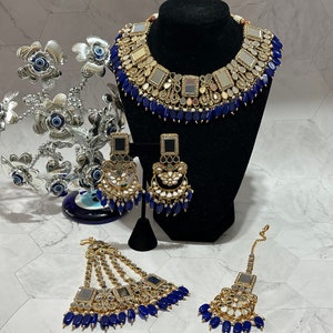 May include: A gold and silver Indian bridal jewelry set with blue beads. The set includes a necklace, earrings, and a maang tikka.