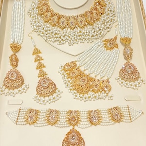 Peut inclure: Un ensemble de bijoux de mariée en or et blanc avec des accents de perles et de pierres précieuses. L'ensemble comprend un collier, des boucles d'oreilles, un maang tikka, un collier ras du cou et un pendentif.