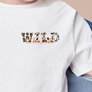 Könnte beinhalten: Weißes T-Shirt mit dem Aufdruck "WILD child" in Leopardenmuster.