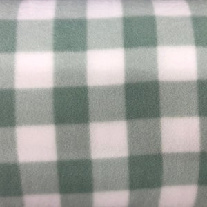 May include: Close-up of a soft, textured fabric with a large gingham pattern. The pattern features alternating squares of white and a muted green color. The fabric appears to be fleece or a similar material, suitable for blankets or apparel.