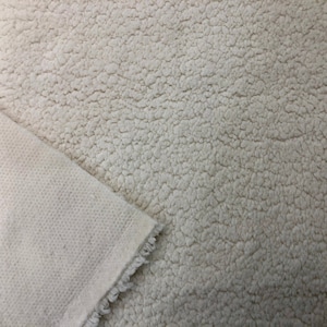 May include: Close-up of a white faux fur fabric with a soft, fluffy texture. The fabric is shown with a plain white backing.