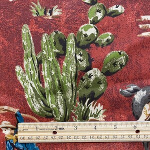 May include: Red fabric with a repeating pattern of green cactus plants and cowboys riding horses. The fabric is measured with a ruler that reads "MADE IN CHINA".