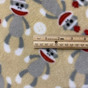 May include: Beige fleece fabric with a repeating pattern of gray sock monkeys wearing red hats. A ruler is placed on the fabric, showing the measurement of 30 inches.