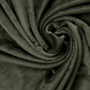 May include: Close-up of olive green corduroy fabric. The fabric is folded and draped, showcasing the ribbed texture and subtle variations in color. The fabric has a soft, velvety appearance.