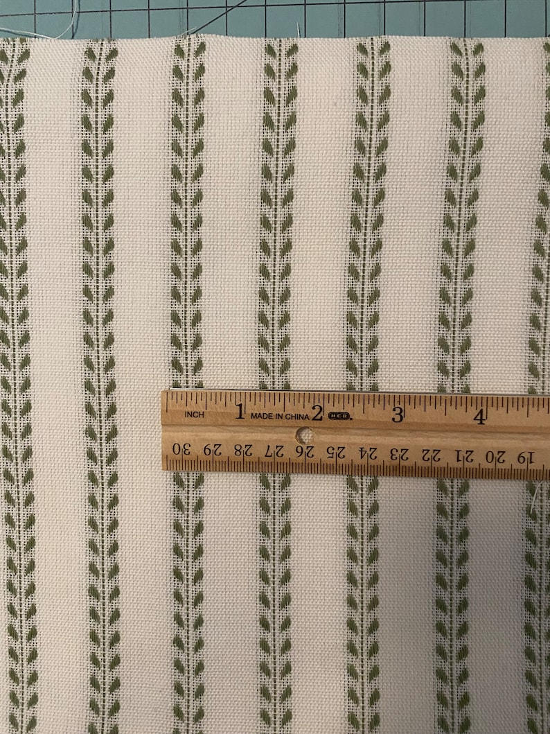 May include: White fabric with green leaf-shaped stripes. A ruler is placed on the fabric, showing the stripes are 2.5 cm apart.