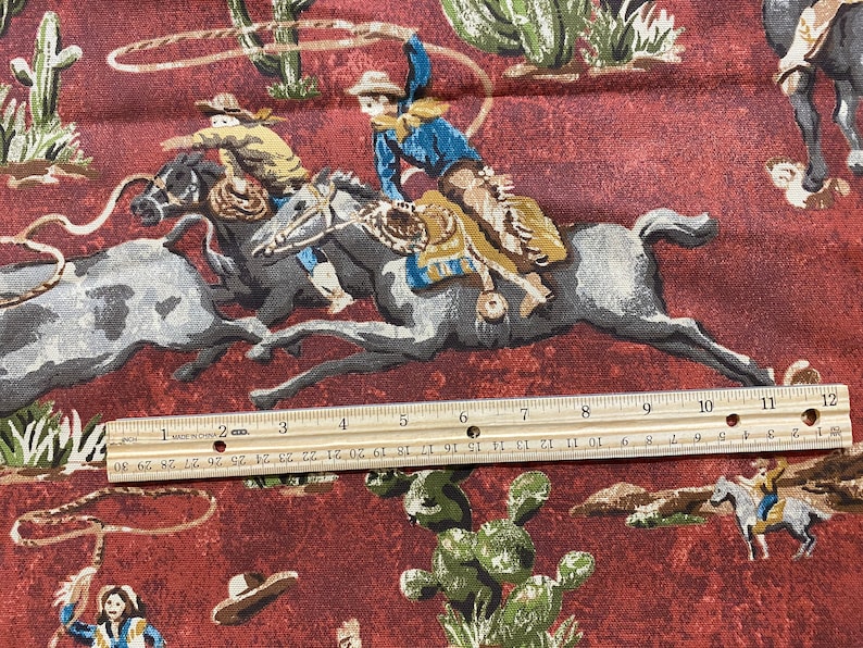 May include: A red fabric with a repeating pattern of cowboys riding horses. The cowboys are wearing hats and boots. The horses are brown and white. The fabric has a rustic, vintage look.
