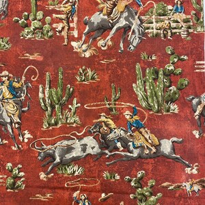 May include: A red fabric with a repeating pattern of cowboys riding horses and bulls, cacti, and lasso ropes. The cowboys are wearing blue, brown, and white clothing. The fabric has a vintage look.