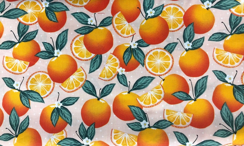 Op de afbeelding: Een roze stof met een herhalend patroon van sinaasappelschijfjes en hele sinaasappelen met groene bladeren. De sinaasappelen hebben een gele kern en een rood-oranje schil.