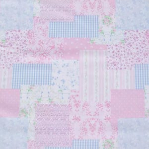 May include: A patchwork textile featuring a variety of patterns in shades of pink and blue. The design includes floral prints, polka dots, gingham checks, and striped patterns, creating a visually diverse and textured surface.