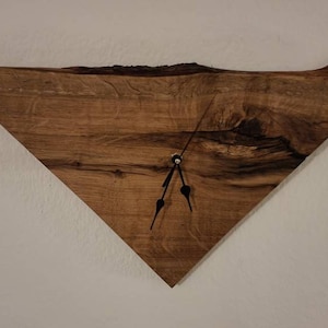 May include: A triangular wooden clock with black hands on a white wall.