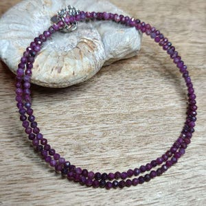 Könnte beinhalten: Eine doppelreihige Halskette aus kleinen, facettierten violetten Edelsteinperlen. Die Halskette liegt auf einer Holzoberfläche.