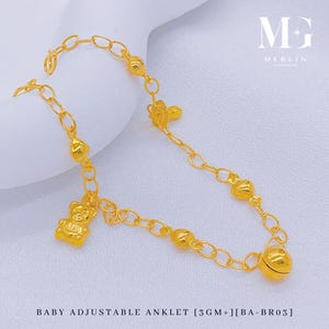 May include: A gold baby adjustable anklet featuring a teddy bear charm, heart-shaped beads, and a bell. The anklet is made of linked chain and has the text "BABY ADJUSTABLE ANKLET [3GM+] [BA-BR03]" at the bottom.