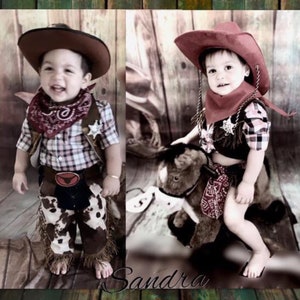May include: Two toddlers dressed in cowboy costumes. One is wearing a plaid shirt, brown pants with fringe, a red bandana, and a brown cowboy hat. The other is wearing a plaid shirt, a red bandana, and a red cowboy hat. They are both smiling.