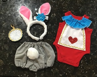 May include: A costume set including a white and pink bunny ear headband with a blue flower, a red sleeveless bodysuit with a white bib featuring a red heart, gray bloomers with a white tail, and a round gold-rimmed clock pendant.