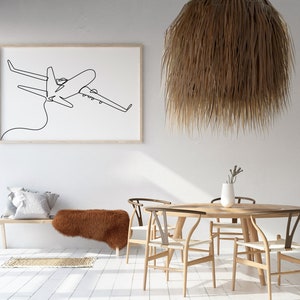 May include: A white wall with a framed black and white line drawing of an airplane. A wooden bench with a brown faux fur throw is in the foreground. A round wooden table with four wooden chairs is in the center of the room. A large, brown, woven pendant light hangs above the table.