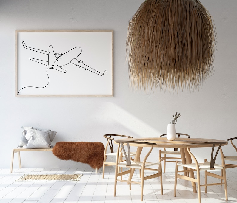 May include: A white wall with a framed black and white line drawing of an airplane. A wooden bench with a brown faux fur throw is in the foreground. A round wooden table with four wooden chairs is in the center of the room. A large, brown, woven pendant light hangs above the table.