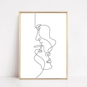 May include: A framed minimalist art print featuring a continuous line drawing of two faces in profile, one above the other. The artwork is rendered in black against a white background, encased in a gold-colored frame.